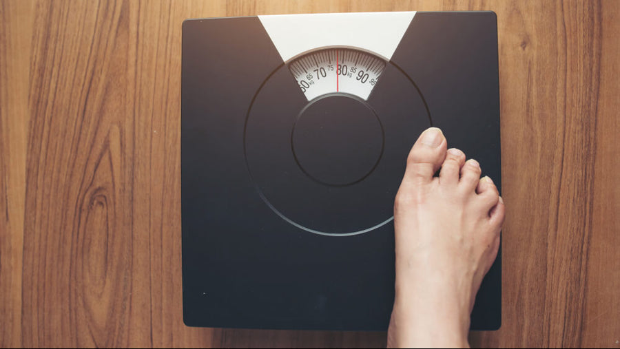 A person's feet visible stepping onto a bathroom scale showing the frustration of why am i not seeing results from working out when the number on the scale is not moving.