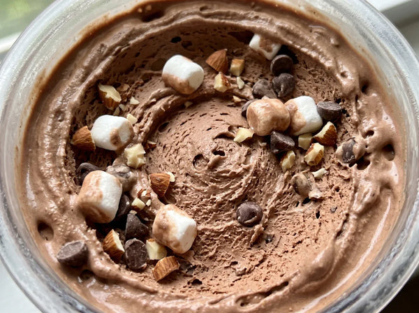 Close-up of Rocky Road protein ice cream in a Ninja Creami pint, with marshmallows, chopped almonds, and chocolate chips mixed into creamy chocolate base.
