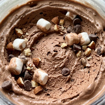 Close-up of Rocky Road protein ice cream in a Ninja Creami pint, with marshmallows, chopped almonds, and chocolate chips mixed into creamy chocolate base.