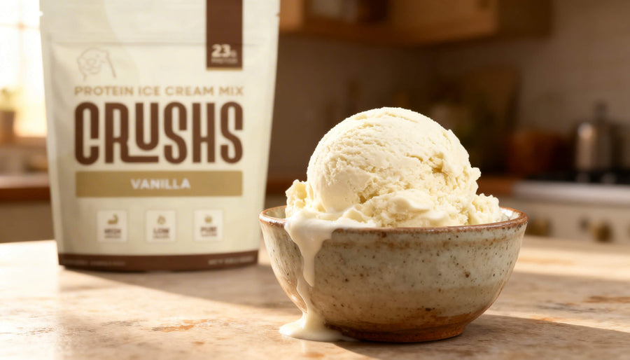 A creamy scoop of vanilla allulose ice cream in a speckled ceramic bowl with a CRUSHS Protein Ice Cream Mix bag in the background.
