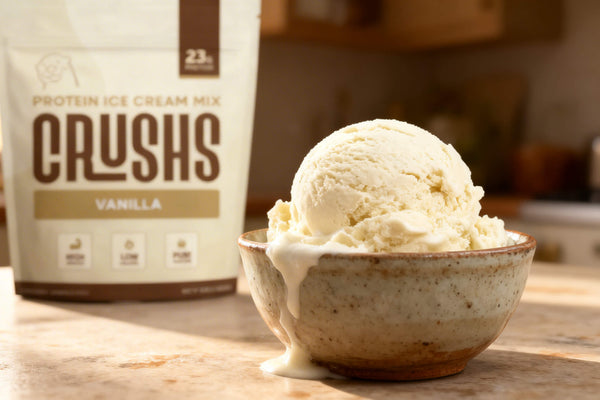 A creamy scoop of vanilla allulose ice cream in a speckled ceramic bowl with a CRUSHS Protein Ice Cream Mix bag in the background.
