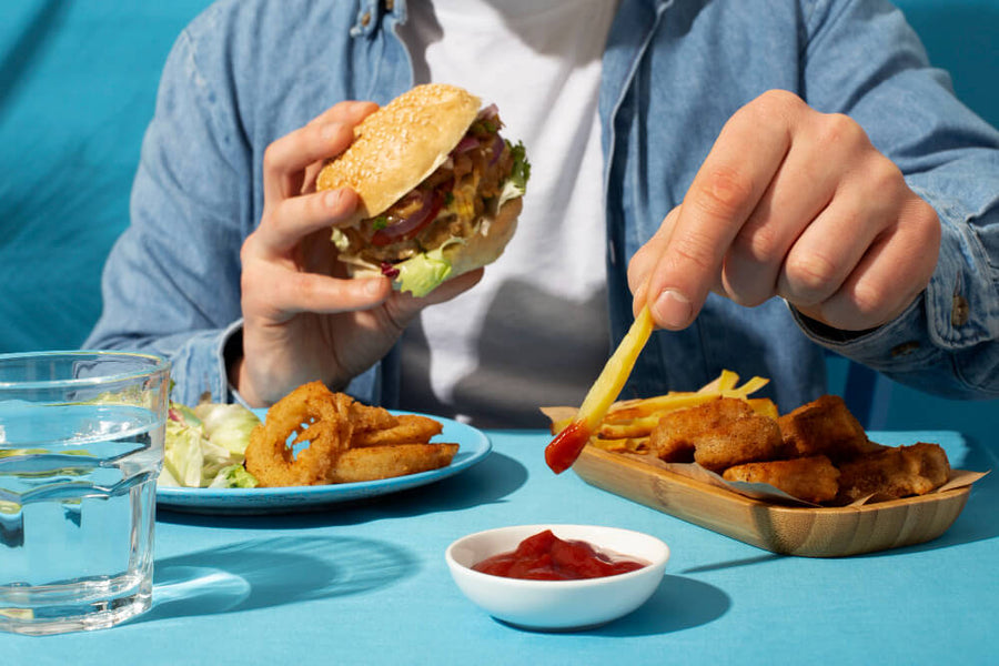 Person holding a burger and fries at a meal, representing high-fat fast food as one of the bad foods to eat before bed Caption: High-fat, heavy meals close to bedtime keep your digestive system working when it should be winding down.