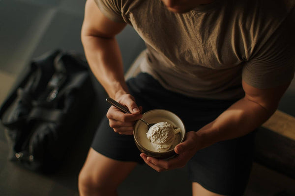 A fit man's torso in gym clothes sitting down holding a bowl representing the post workout nutrition moment that eating ice cream after a workout is designed to replace with something more enjoyable.