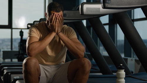 A fit person's torso in gym clothes sitting on a gym bench looking frustrated representing the common outcome of consistent training undermined by fitness nutrition mistakes happening outside the gym.