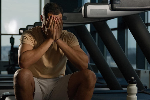 A fit person's torso in gym clothes sitting on a gym bench looking frustrated representing the common outcome of consistent training undermined by fitness nutrition mistakes happening outside the gym.