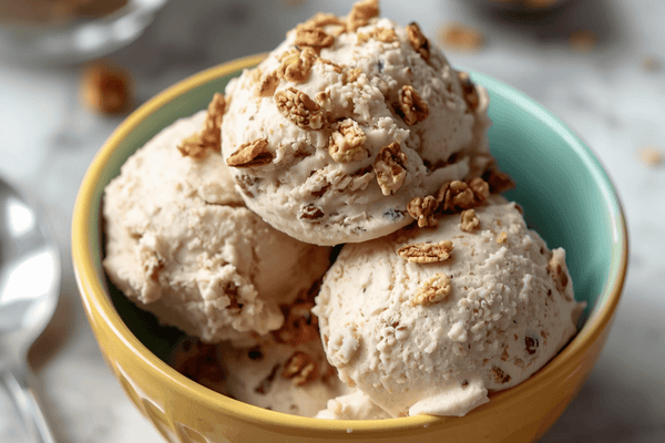 A scoop of creamy ice cream topped with granola clusters in a ceramic bowl showing healthy mix ins that add crunch without spiking sugar.