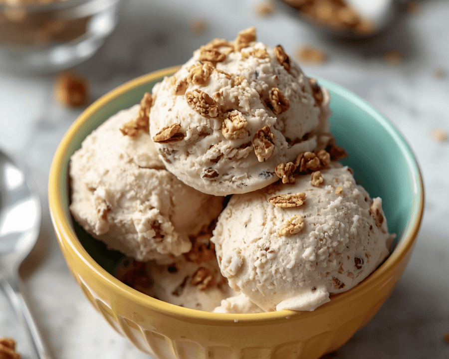 A scoop of creamy ice cream topped with granola clusters in a ceramic bowl showing healthy mix ins that add crunch without spiking sugar.