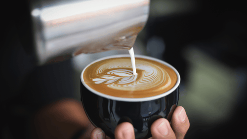 A hot latte with latte art in a black cup as a collagen peptide high protein coffee idea.