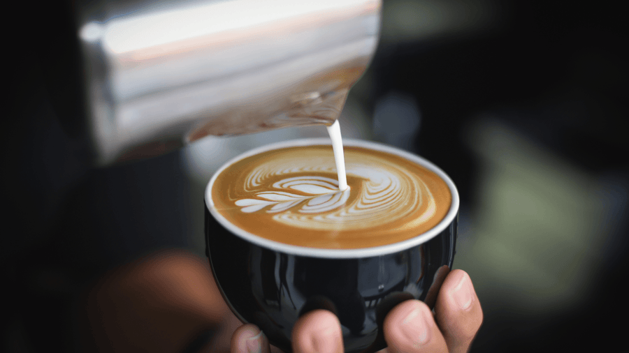 A hot latte with latte art in a black cup as a collagen peptide high protein coffee idea.