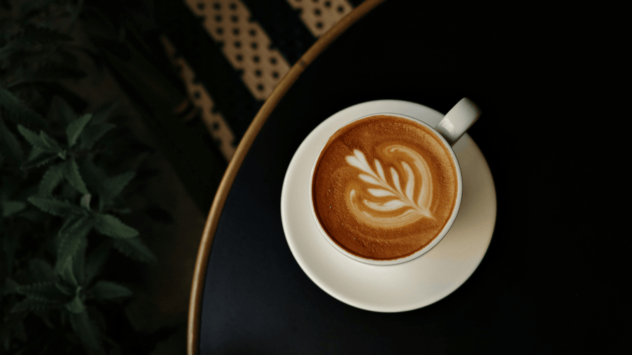 An overhead shot of a latte with latte art on a dark tray showing how much caffeine per cup in an espresso-based drink.
