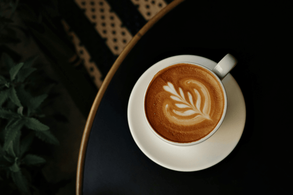 An overhead shot of a latte with latte art on a dark tray showing how much caffeine per cup in an espresso-based drink.
