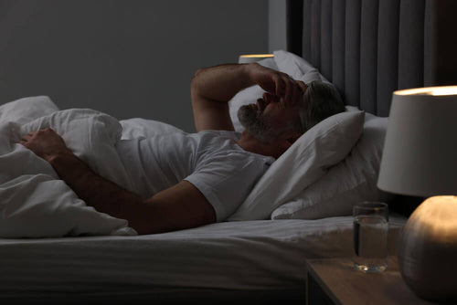 Person lying awake in bed at night with hand on forehead, representing poor sleep quality and its impact on fitness and fat loss results.