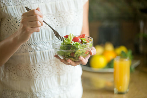 Person holding a clear bowl of fresh salad with vegetables and a fork.