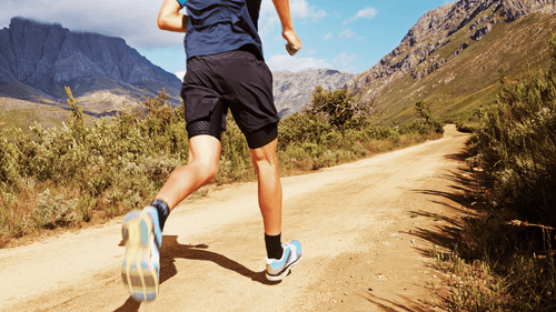 A man's torso and legs visible running on a mountain trail outdoors representing the active cardio habits that support how to get ready for summer body through consistent movement and calorie burn.