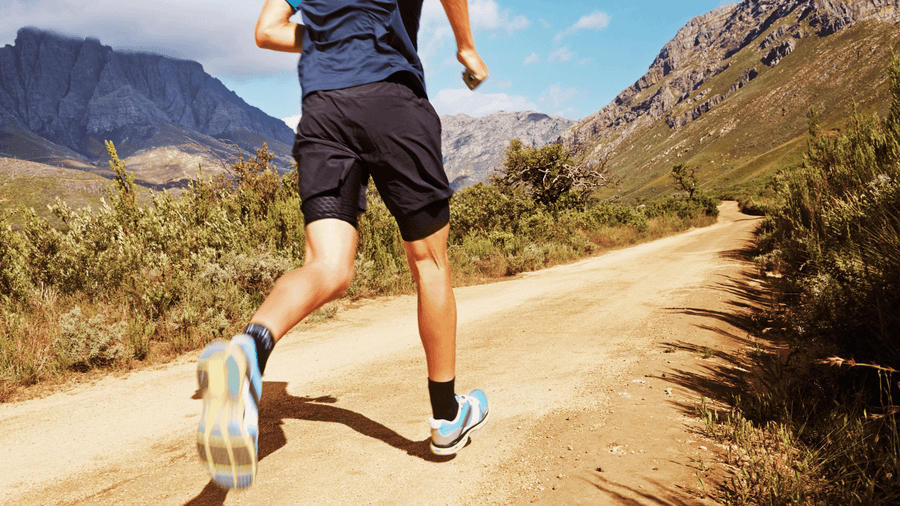 A man's torso and legs visible running on a mountain trail outdoors representing the active cardio habits that support how to get ready for summer body through consistent movement and calorie burn.