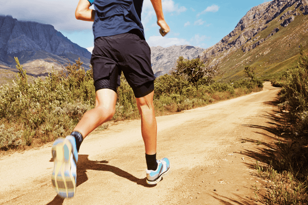 A man's torso and legs visible running on a mountain trail outdoors representing the active cardio habits that support how to get ready for summer body through consistent movement and calorie burn.