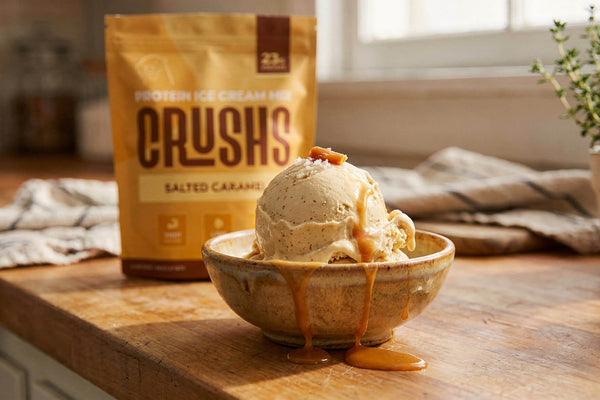 A creamy scoop of salted caramel protein ice cream in a ceramic bowl with a CRUSHS Salted Caramel Protein Ice Cream Mix bag visible behind it representing the answer to is protein ice cream healthy when the ingredients are right.