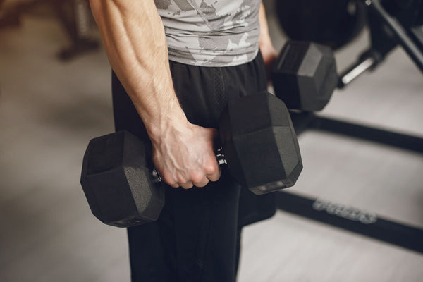 A fit man's torso and arms visible in a gym holding a bowl of protein ice cream representing the importance of leucine post workout for muscle repair and recovery.