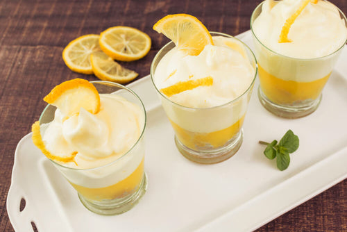 Lemon yogurt parfait glasses with whipped cream and lemon slices as a low calorie Mother's Day dessert.