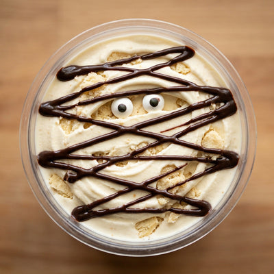 Mummy Wrap Ninja Creami recipe made with CRUSHS vanilla protein ice cream mix, shortbread crumbles, chocolate syrup bandages, and candy eyeballs.