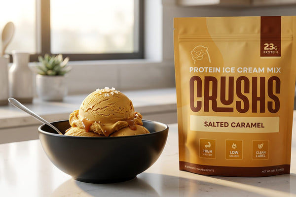A CRUSHS Salted Caramel Protein Ice Cream Mix bag beside a creamy scoop of salted caramel ice cream in a black bowl representing the best protein ice cream mix for Ninja Creami that delivers 23g of protein at 180 calories with 0g added sugar.