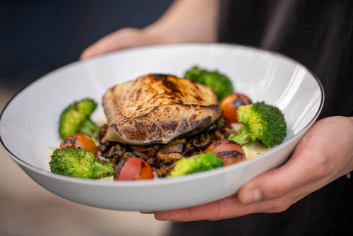 A person's hands holding a bowl of grilled salmon with vegetables and broccoli representing a protein rich meal that helps address the signs you're not eating enough protein through consistent daily intake.