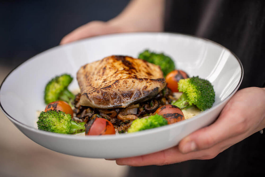 A person's hands holding a bowl of grilled salmon with vegetables and broccoli representing a protein rich meal that helps address the signs you're not eating enough protein through consistent daily intake.