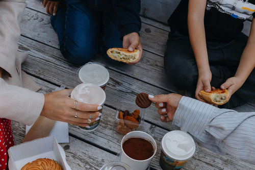 Overhead view of two people sharing small snacks on a wooden surface, with crackers, nuts, and dipping sauces.
