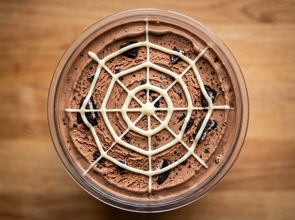 Spiderweb Cookie Ninja Creami recipe made with CRUSHS chocolate protein ice cream mix, crushed chocolate sandwich cookies, and a white chocolate spiderweb.