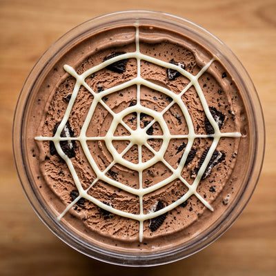 Spiderweb Cookie Ninja Creami recipe made with CRUSHS chocolate protein ice cream mix, crushed chocolate sandwich cookies, and a white chocolate spiderweb.