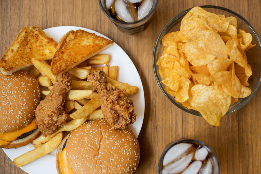 Overhead view of junk food including a burger, fries, and chips on a wooden table.