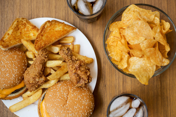 Overhead view of junk food including a burger, fries, and chips on a wooden table.