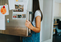 Young woman opening a stainless steel refrigerator door in a home kitchen.