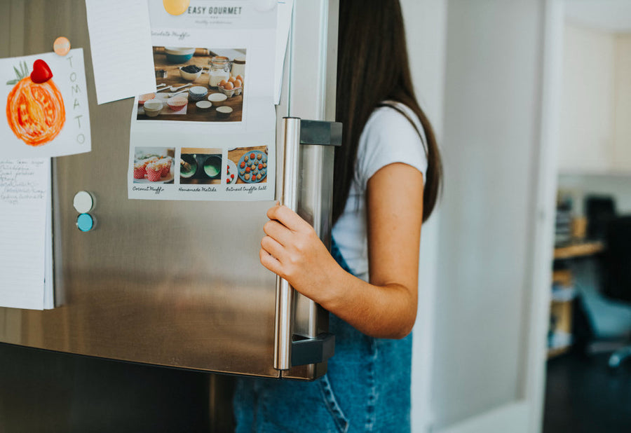 Young woman opening a stainless steel refrigerator door in a home kitchen.