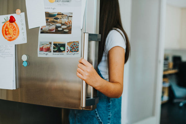 Young woman opening a stainless steel refrigerator door in a home kitchen.