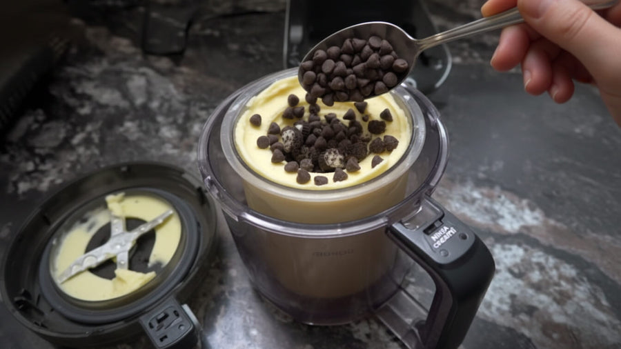 A hand adding mix ins into a Ninja Creami pint container on a kitchen counter showing one of the most useful Ninja Creami tips and tricks for better results.