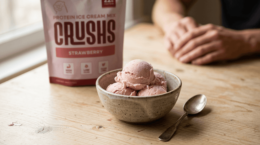 A creamy scoop of strawberry protein ice cream in a ceramic bowl with a CRUSHS Strawberry Protein Ice Cream Mix bag visible beside it representing a high protein dessert habit worth building into getting ready for summer health goals.