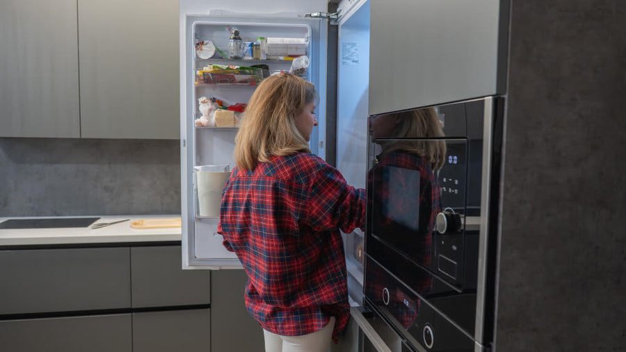 Woman looking into an open refrigerator, representing checking freezer temperature and storage when preparing a Ninja Creami base for freezing.