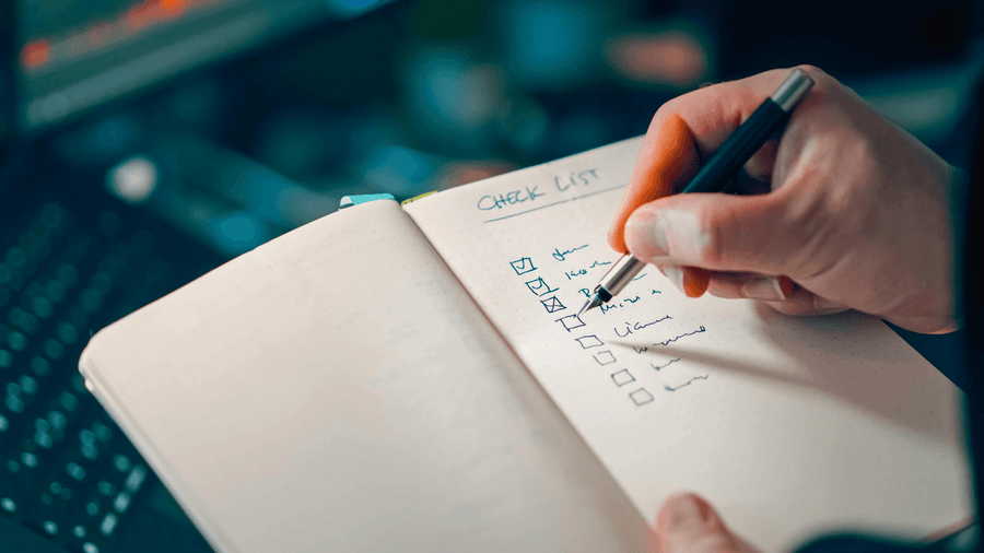 A person's hand writing a checklist in a notebook representing the planning and goal-setting habits behind getting ready for summer body and lifestyle changes that actually stick.