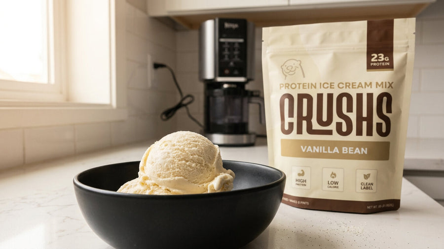 A CRUSHS Vanilla Protein Ice Cream Mix bag beside a creamy scoop of vanilla protein ice cream in a black bowl with a Ninja Creami machine visible in the background showing the easiest way to make protein ice cream Ninja Creami style.
