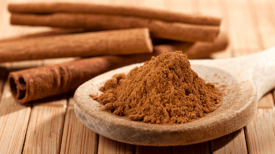 A wooden bowl of ground cinnamon with cinnamon sticks as a healthy add-in for coffee to moderate blood sugar.