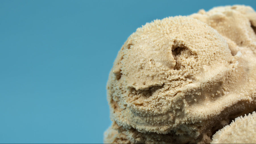A creamy scoop of freshly spun protein ice cream recipe ninja creami result in a rustic ceramic bowl, slightly melting, warm kitchen background.