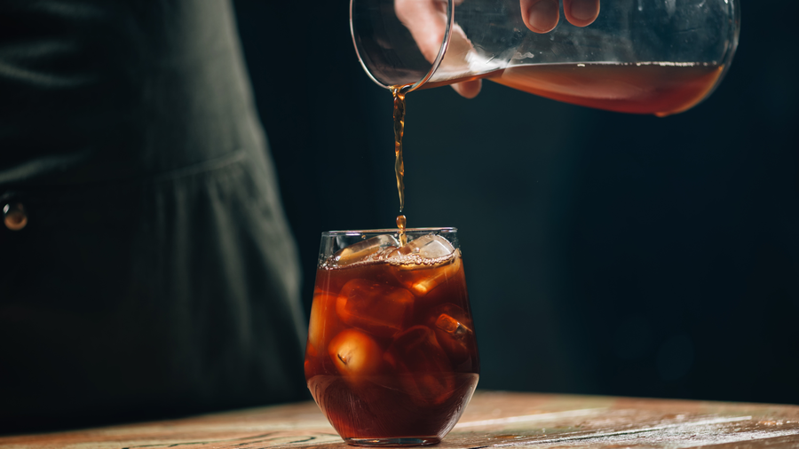 Cold brew coffee being poured over ice in a glass showing the difference in cold brew vs iced coffee caffeine and brew method.