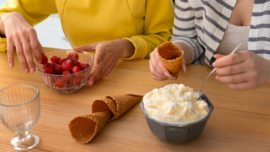 Two people's torsos and hands visible eating ice cream from bowls and cones at a table with fresh berries beside them showing that is protein ice cream healthy enough to enjoy regularly without the guilt of traditional dessert.