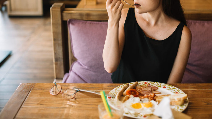 A woman's torso visible eating a large meal at a table representing the all-or-nothing thinking pattern that makes how to make healthy eating habits stick so difficult for most people.