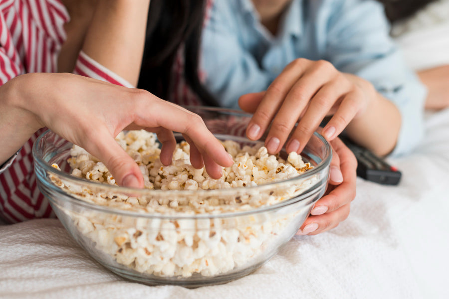 Two people reaching into a bowl of popcorn together.