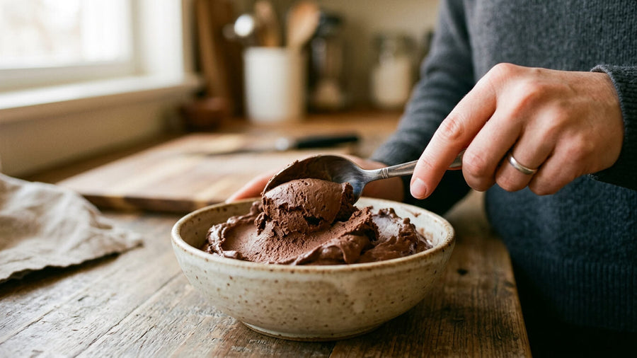 A person's hand scooping chocolate protein ice cream from a ceramic bowl in a cozy kitchen showing the real dessert experience at the center of the protein ice cream vs regular ice cream debate.
