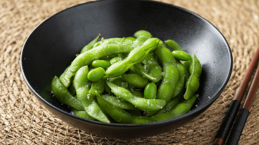 A bowl of steamed edamame pods in a dark pan representing one of the best high protein snacks for summer that is plant-based, portable, and delivers around 17g of protein per cup.