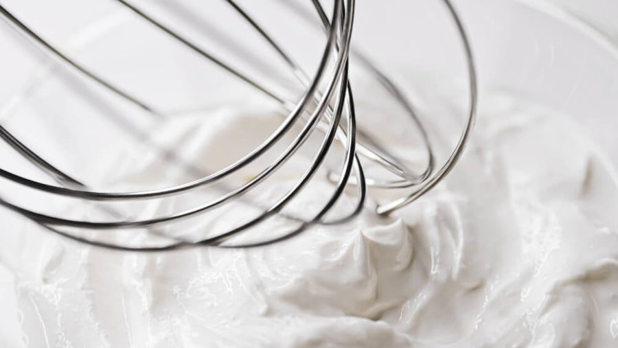 Heavy whipping cream being whisked in a glass bowl.
