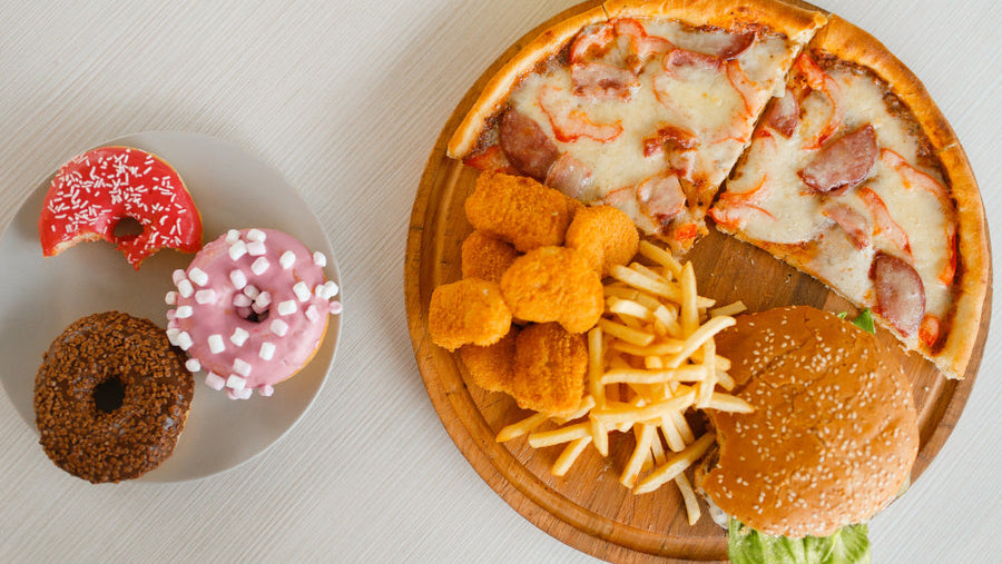 Plate of rich heavy foods like pizza, fries, and donuts that can worsen nausea